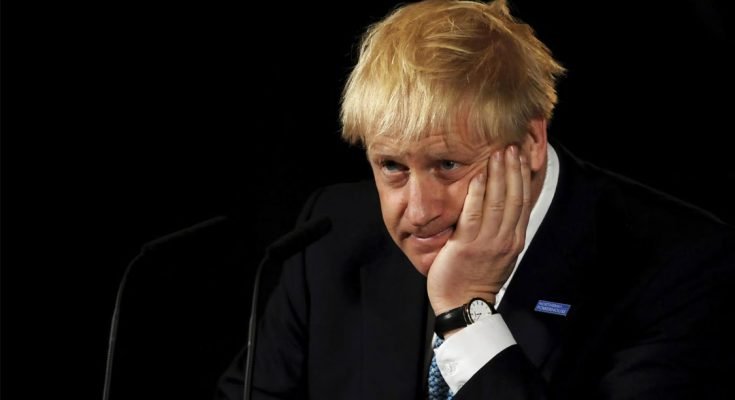 A forlorn looking Boris Johnson sits in front of a microphone against a black background