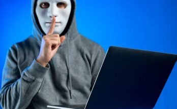 A hacker holding a laptop while wearing a white mask