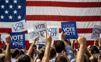 People holding up signs saying "Vote" in front of a US flag